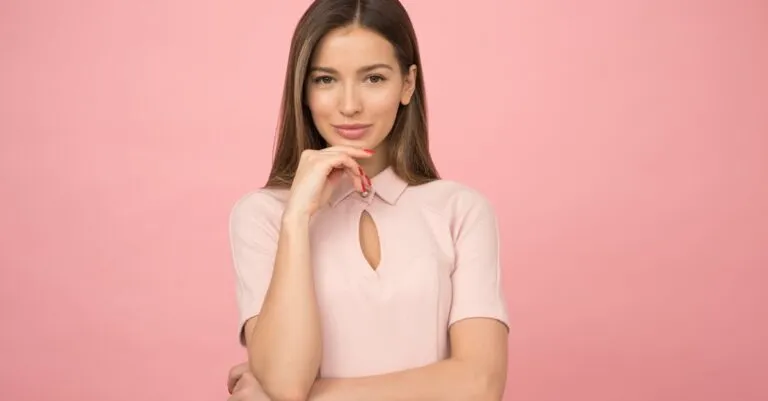 Portrait of a young woman posing elegantly in a studio with a pink background.