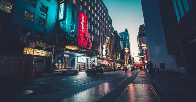 Dynamic urban scene in New York City captured at dusk, highlighting illuminated skyscrapers and lively streets.