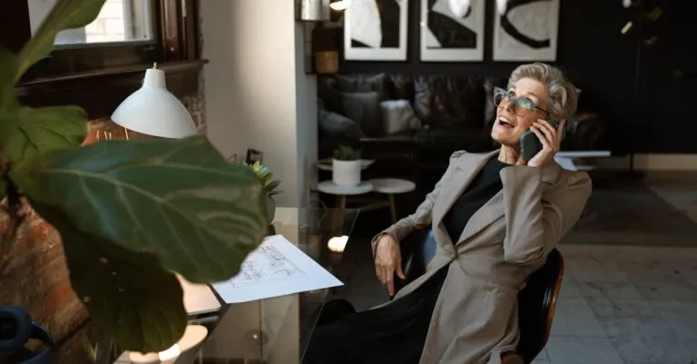 Senior woman in a modern office setting, smiling while on a phone call. Stylish and professional workspace.