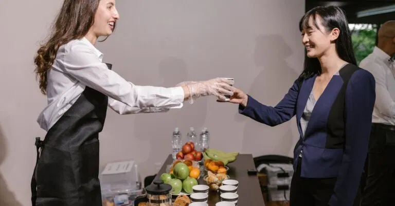 Two professionals interacting at a catered business event with coffee and fruit.