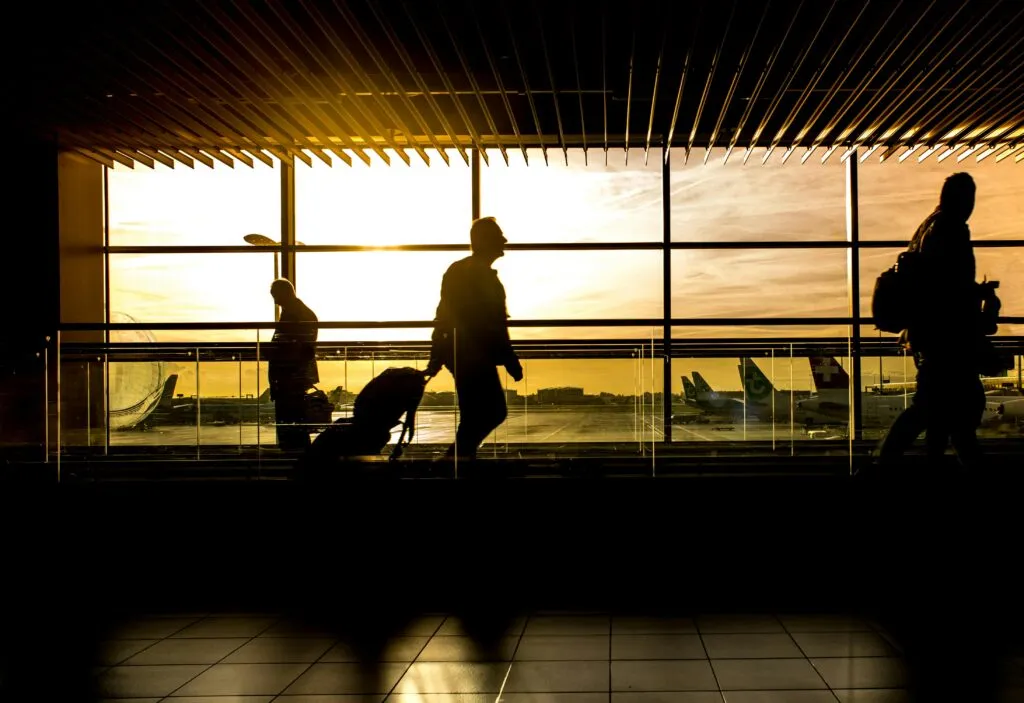 Travelers in silhouette pulling luggage at the airport during a beautiful sunset.