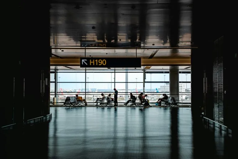 Silhouetted travelers waiting at Shanghai airport terminal gate H190 with cityscape view.