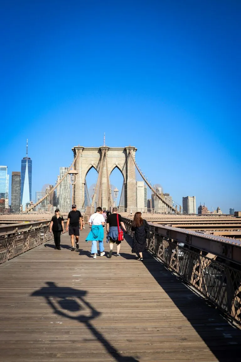 Tourists enjoying a sunny day walk on the iconic Brooklyn Bridge, NYC.
