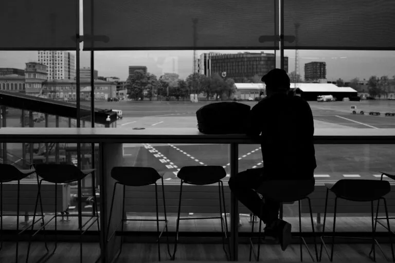 Black and white image of a man sitting in front of airport window in Dubai, United Arab Emirates, observing the runway.