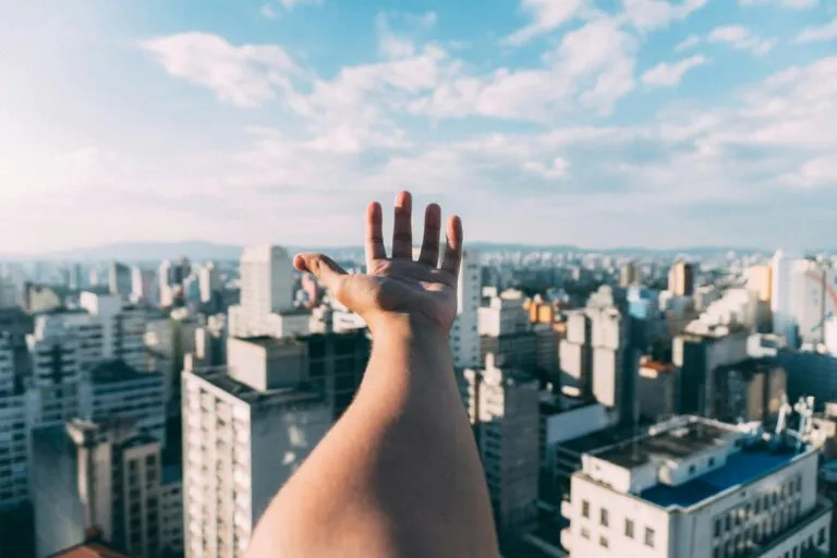 An outstretched hand reaching towards a sunny cityscape, capturing the vibrant skyline and skyscrapers.