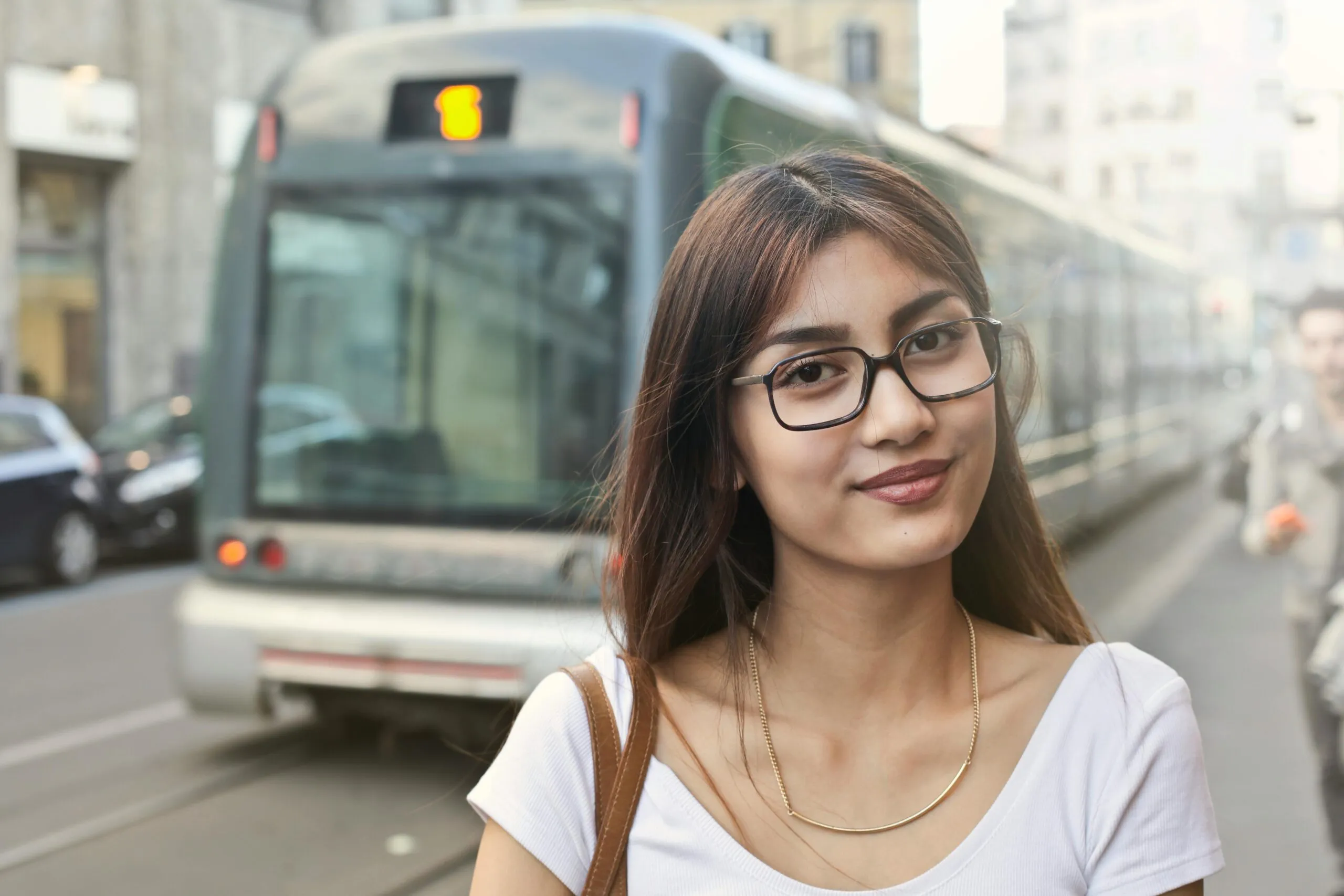 Young woman smiling in front of a tram in Milan, Italy, blending urban style with charm.