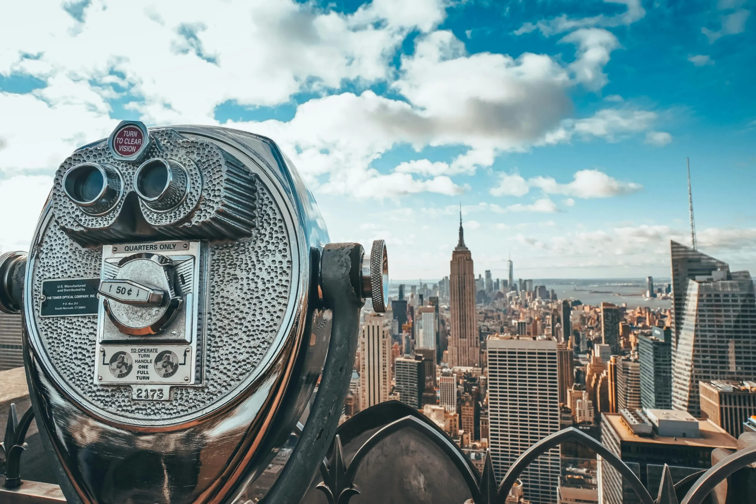 View of New York City skyline featuring iconic Empire State Building with observation binoculars in the foreground.