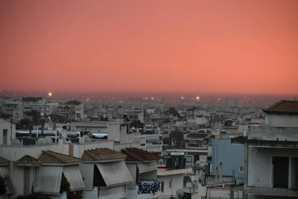 Captivating view of Athens cityscape under a vibrant red sunset sky, showcasing urban architecture.