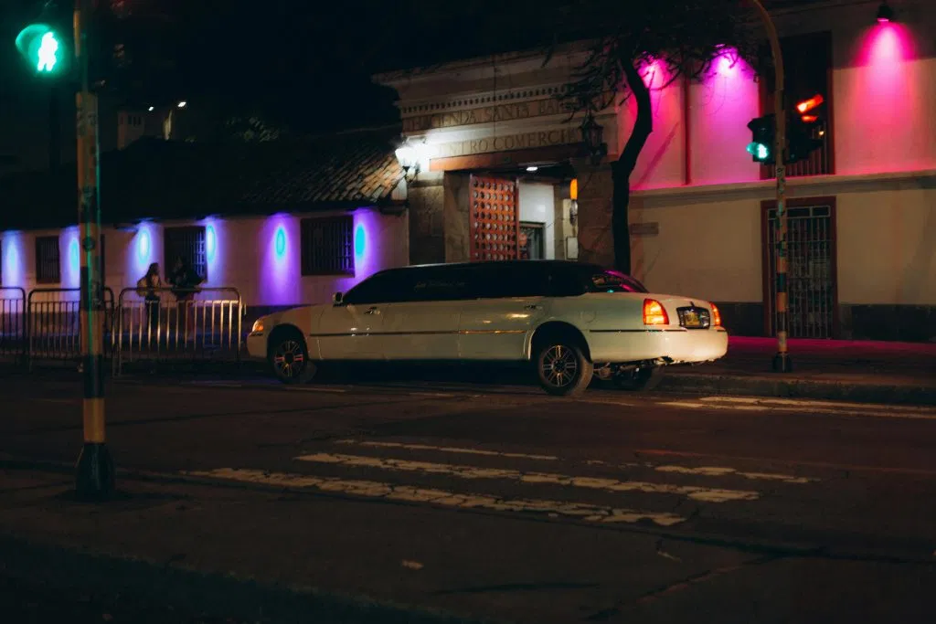 White limousine parked on a city street at night illuminated by colorful neon lights.